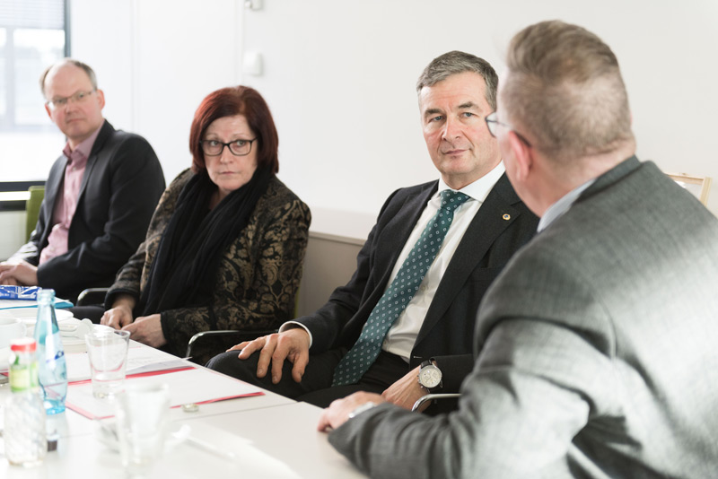 3 Männer und eine Frau im Gespräch an einem Konferenztisch.