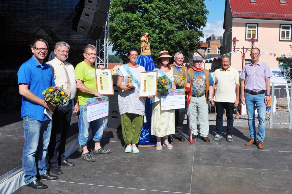Die neuen und alten Preisträger des Wandernden Heilkräuterpreis der Stadt Königsee-Rottenbach sowie Vertreter von Stadt sowie Hofmann & Sommer stehen auf einer Büchne.