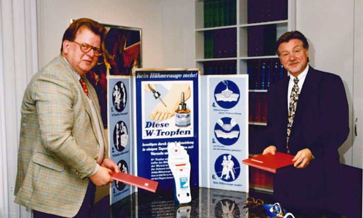 Zwei Personen präsentieren vor einem alten Werbeschild einen Kaufvertrag.